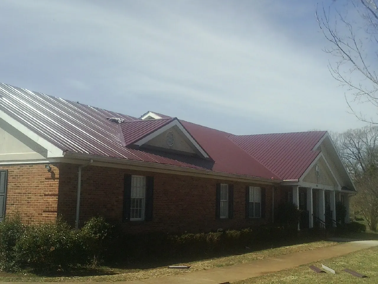 Red metal roof with gabled entries on a long brick building, from a Hail Damage Roof Repair job in Gardiner